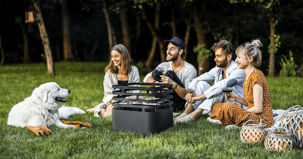 group of four young people and a dog sitting on a lush green lawn at a party