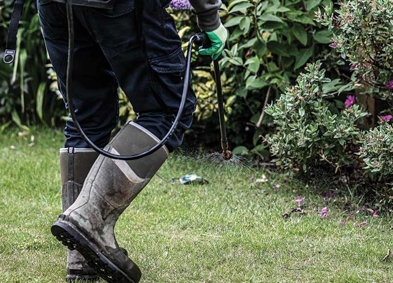 person wearing heavy boots while working in a yard and spraying concentrates on the lawn